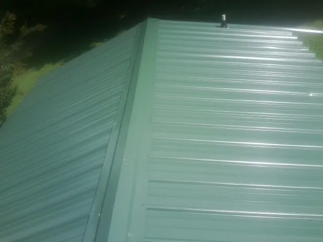 New green metal panels meeting at the ridge of a roof — Flat Roof Repair work by our crew in Norfolk